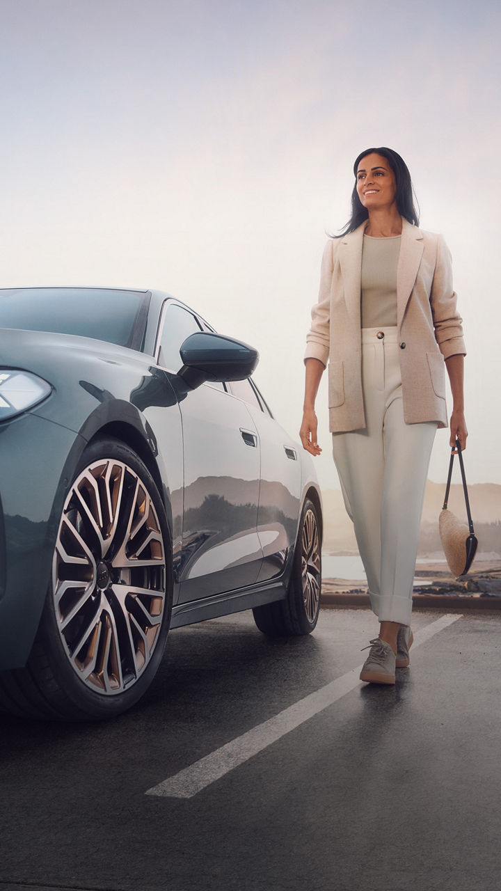 Eine Frau steht neben einem blauen Audi Modell und öffnet die Fahrertür bei weichem Abendlicht.