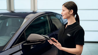 Zwei Männer schauen auf ein Tablet mit einem Audi vor sich, bei dem die Motorhaube auf ist