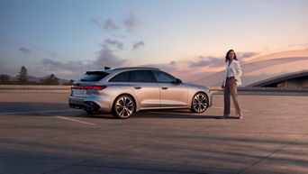 Eine Frau steht neben einem silbernen Audi Modell bei Sonnenuntergang und guckt in die Ferne.