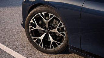 Nahaufnahme einer schwarzen Audi Felge mit silbernem Speichendesign an einem dunkelblauen Fahrzeug.