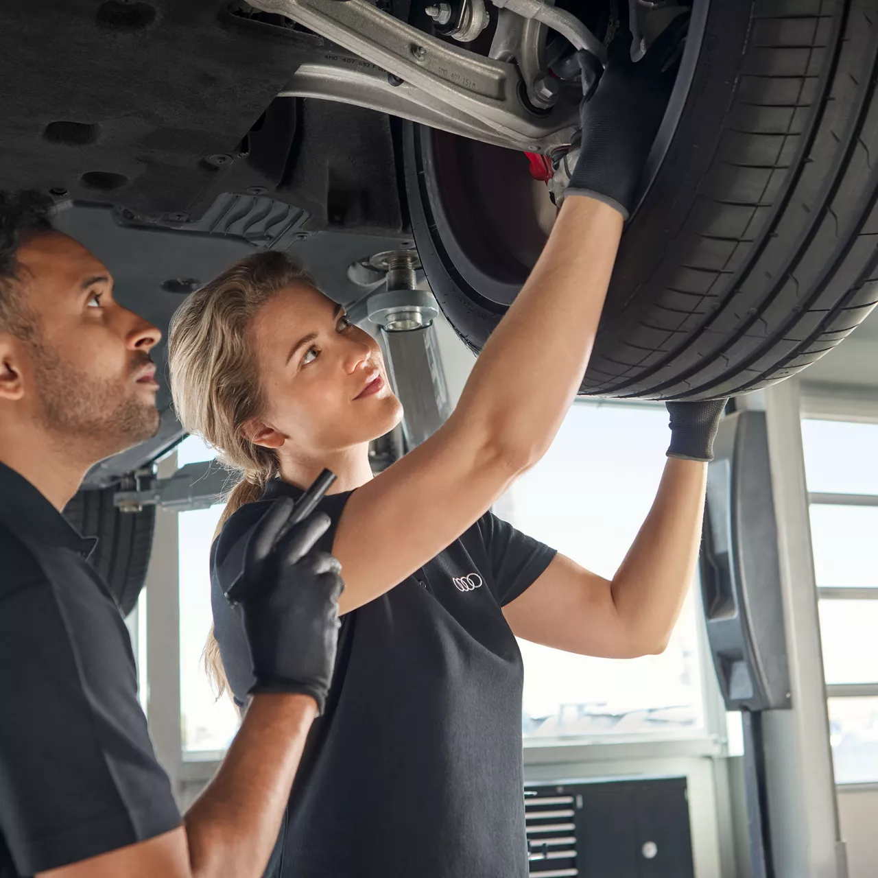 Ein Mann und eine Frau arbeiten an einem Audi auf der Hebebühne